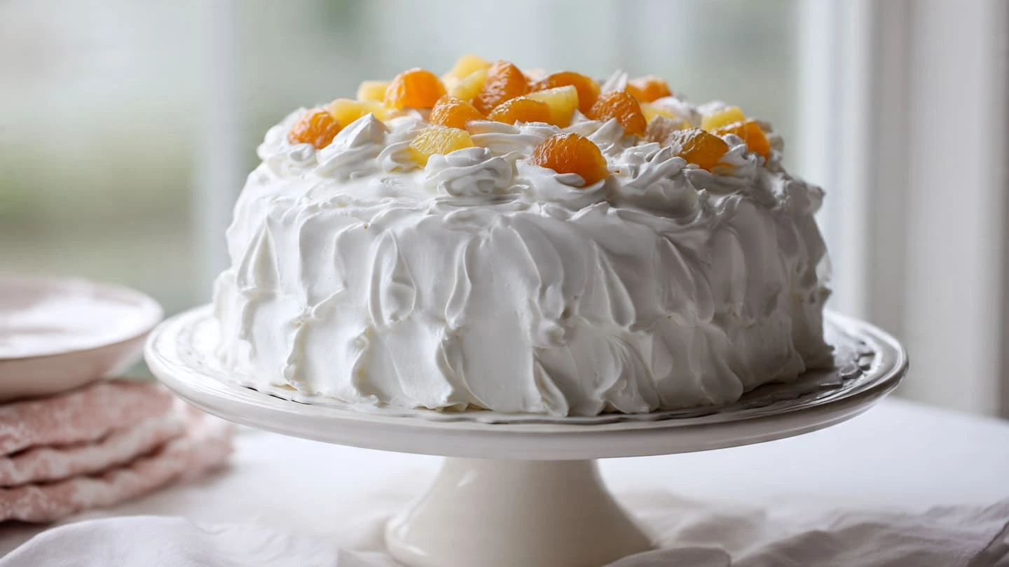 Southern Pig Pickin’ Cake on a cake stand with whipped frosting and fruit